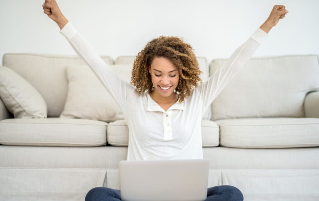 Woman looking at her laptop computer with her arms up in the air celebrating Some Of The Greatest Truths About Successful Entrepreneurs: Be Honest, Be Intentional About Your Spending & Celebrate Your Wins!