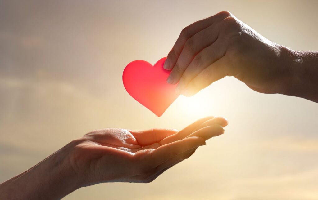 One person placing a heart into the hand of another person, giving a charitable donation to honor someone is a gift that is thoughtful and keeps on giving too.
