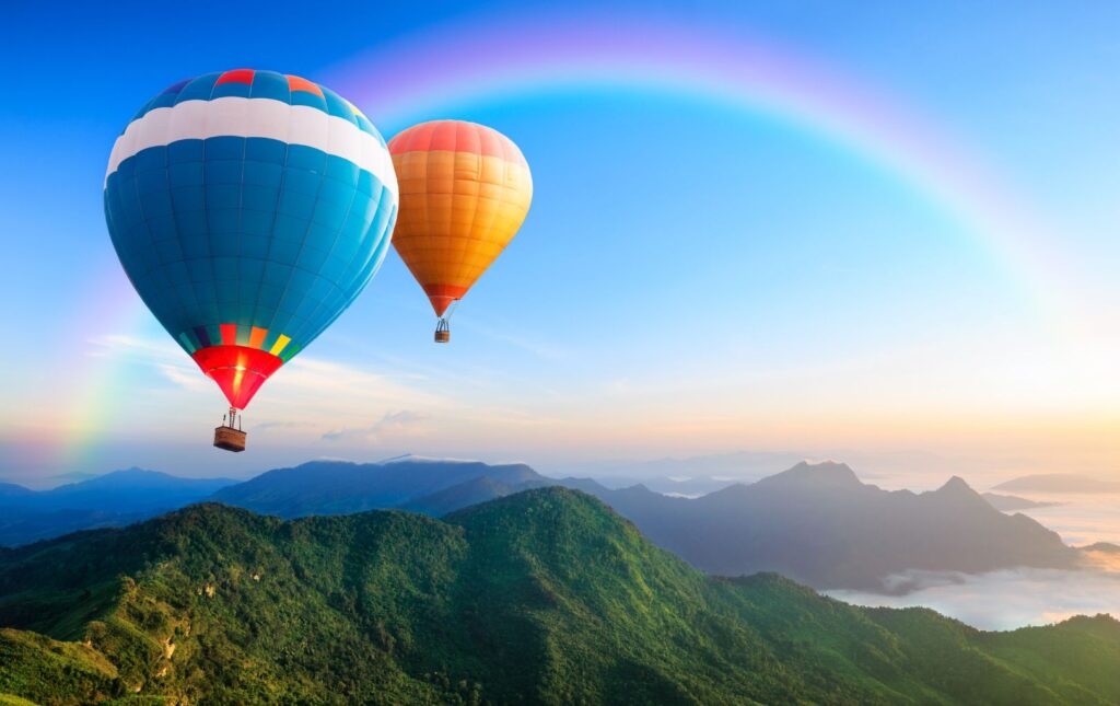 Two Hot Air Balloon Soaring Over The Mountains  With A Rainbow Filled Sky