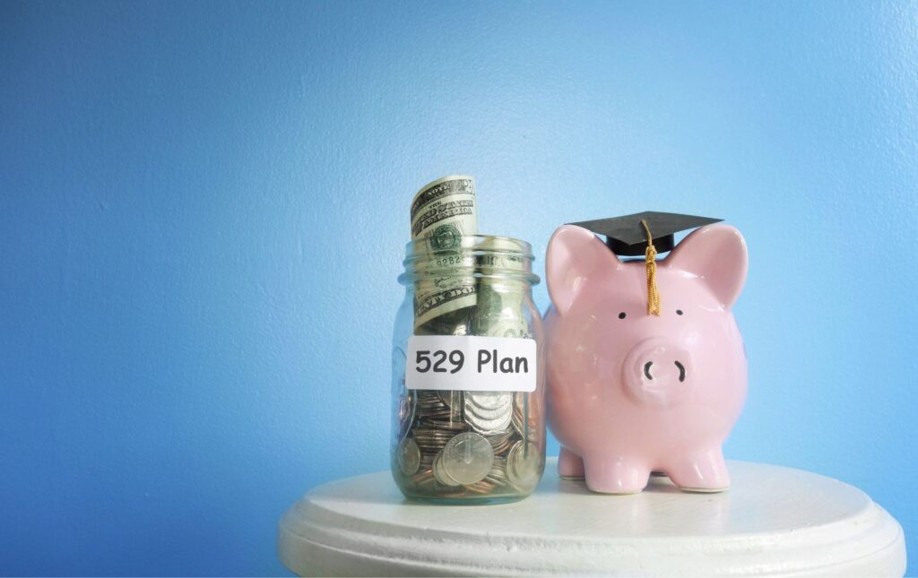 A jar with money for a 529 college savings plan alongside a pink ceramic piggy bank with a graduation cap on its head in between the pig's ears.