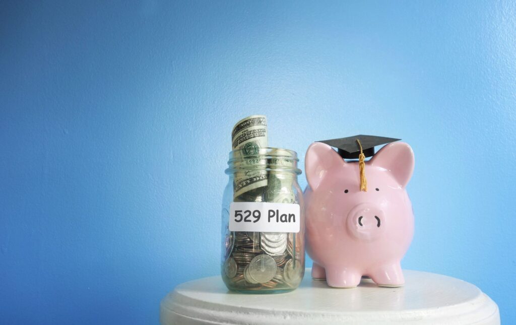 A piggy bank wearing a graduation cap with a mason jar filled with coins and rolled up money for 529 college savings.