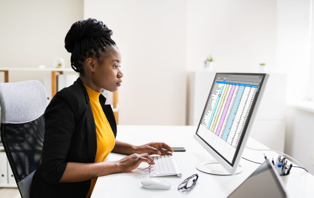 Young adult woman sitting at a computer looking at a spreadsheet to determine her retirement expenses.