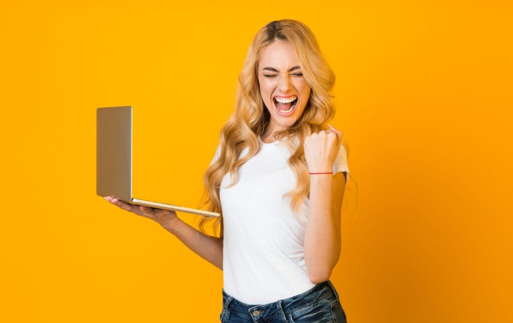 Young adult woman holding a computer in a celebratory pose.