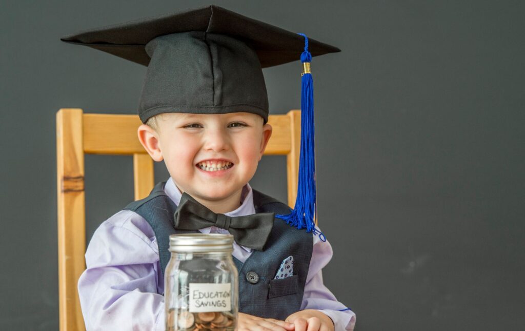 young child in a graduation cap with college savings in an open mason jar filled with coins