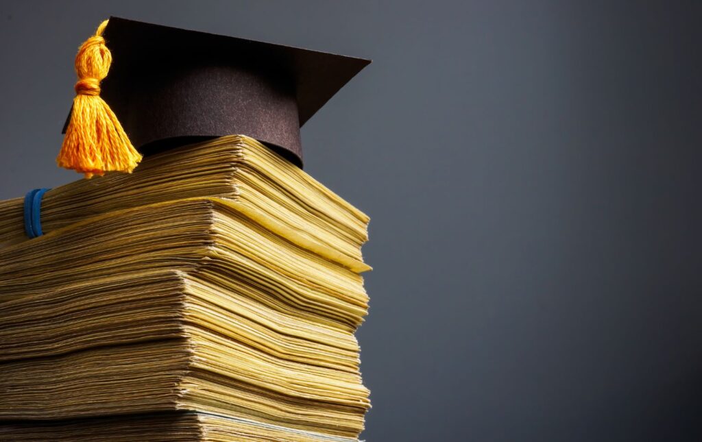 Stacks of money representative of college savings and debt topped of with a graduation cap