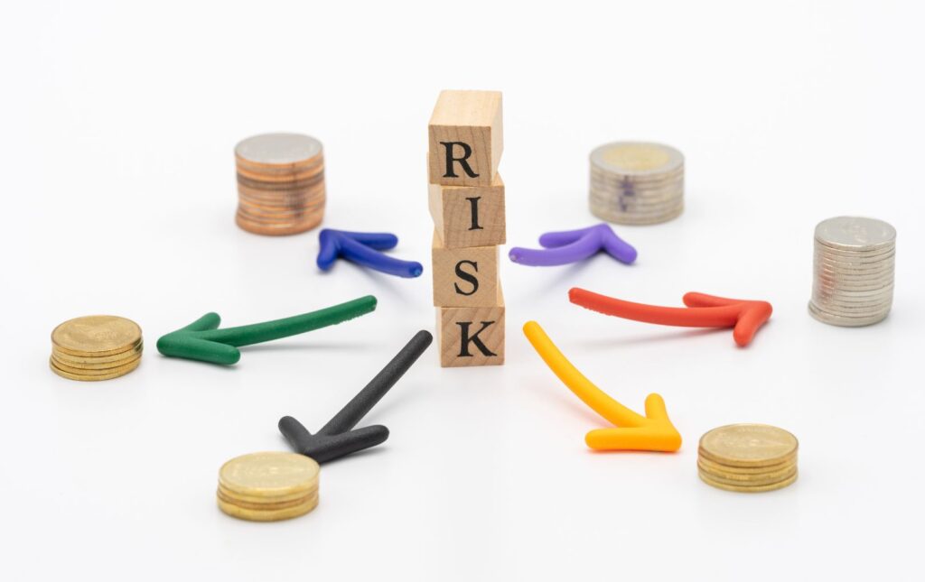 Four dies stacked on one another spelling "RISK" with arrows coming out and stacks of coins representing the mitigation of risk created by money or money to purchase protection to mitigate the risk.