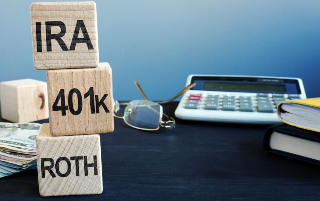 Three die stacked on one another "ROTH," "401k," and IRA with a calculator representing retirement planning.