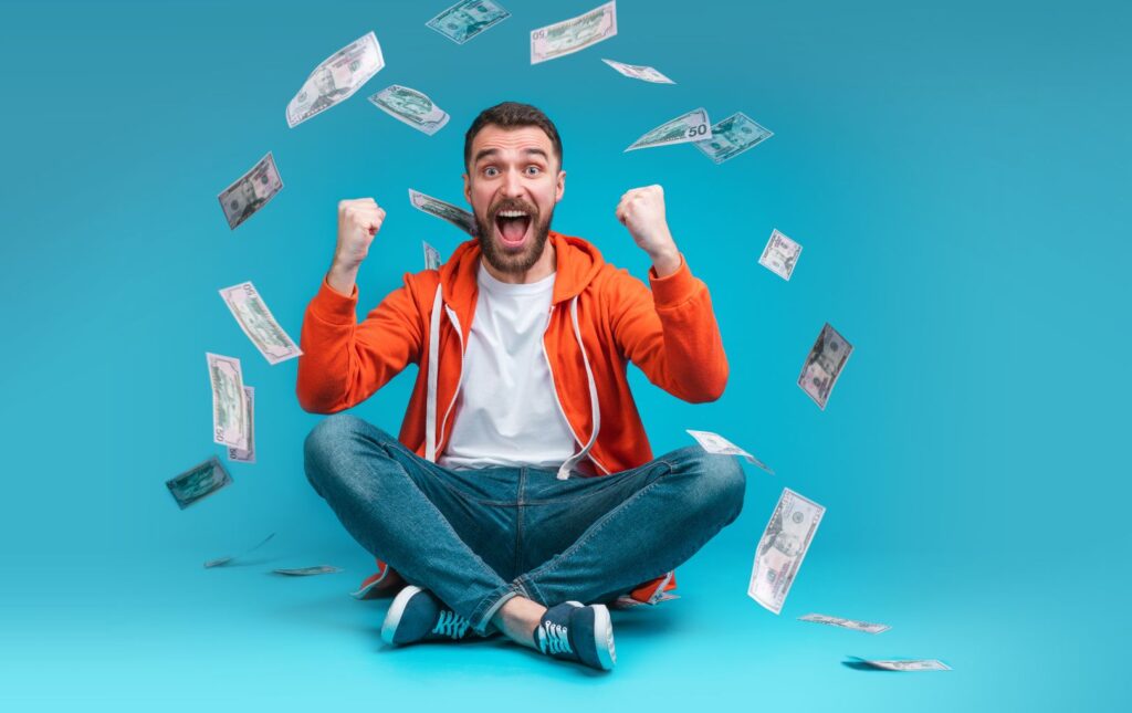 Young man surrounded by paper money "flying in the air" around him celebrating his breaking the cycle of living paycheck-to-paycheck