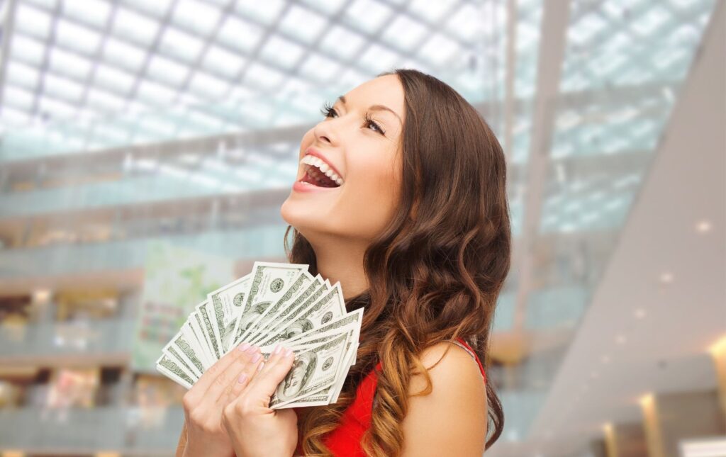 photo of a young woman that looks very happy fanning money and smiling representative of her hoarding cash